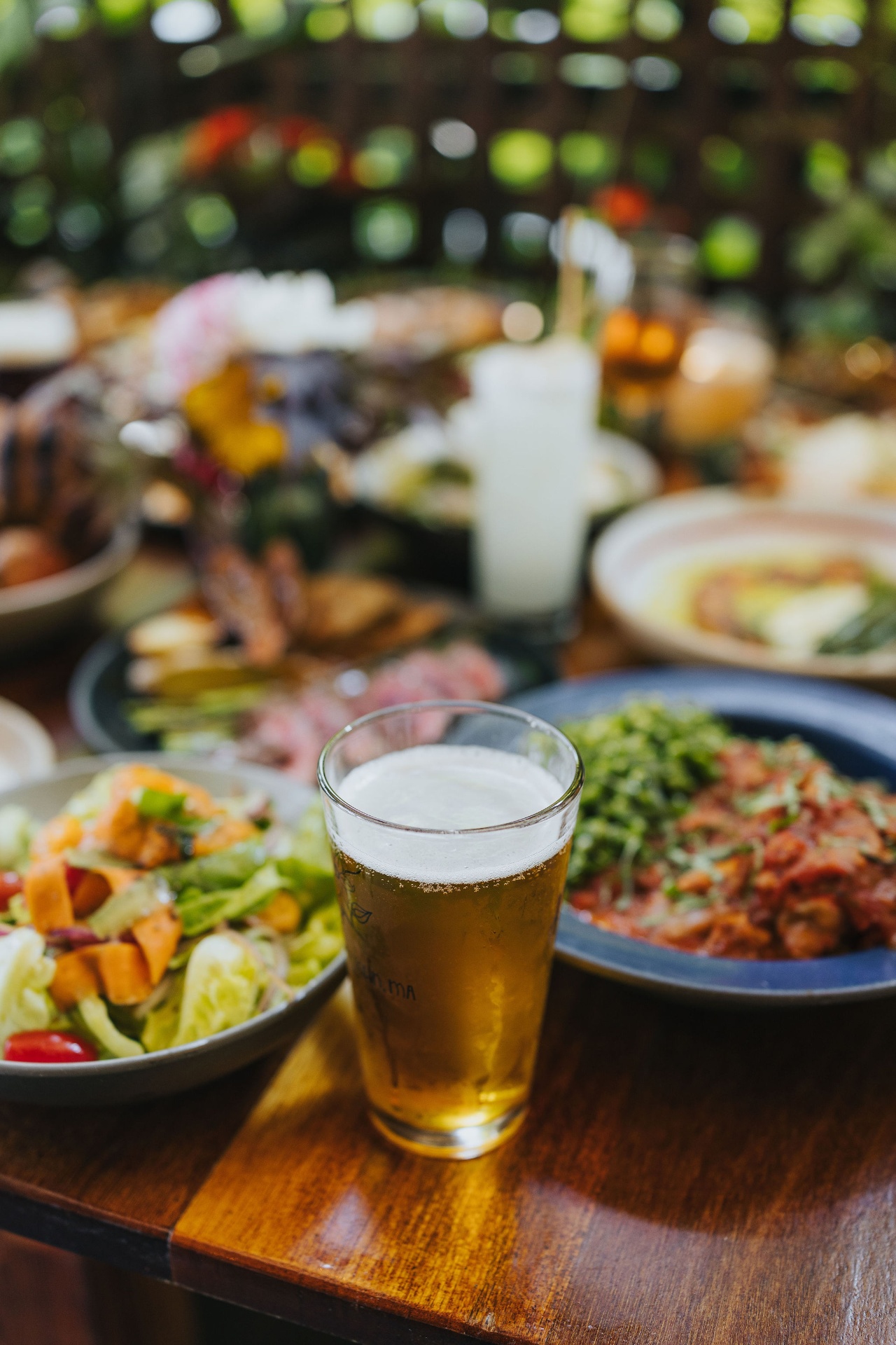 A garden table spread with a cold beer, fresh salad, and shared plates