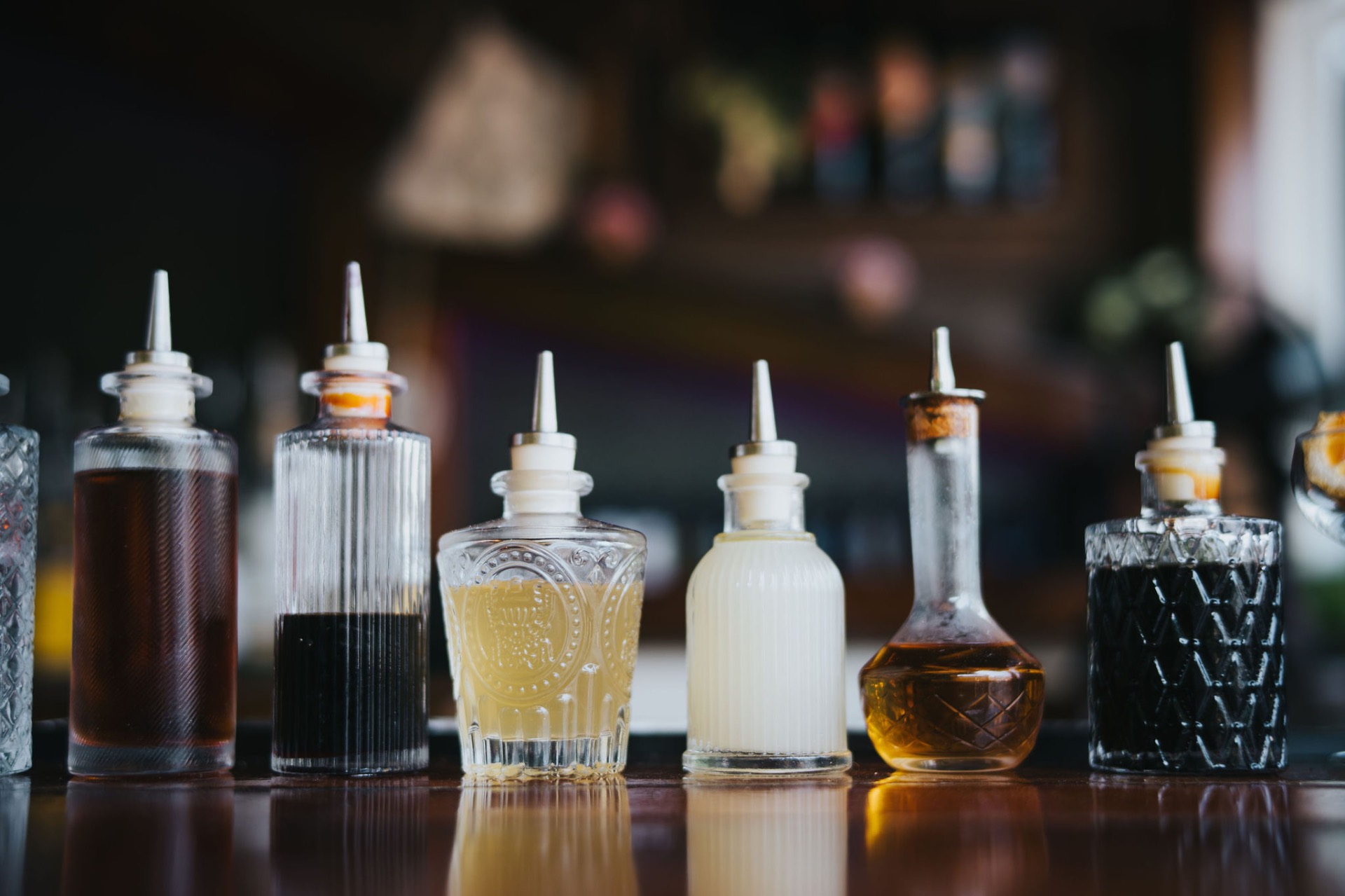 A row of house-made bitters, syrups, and shrubs in vintage glass bottles