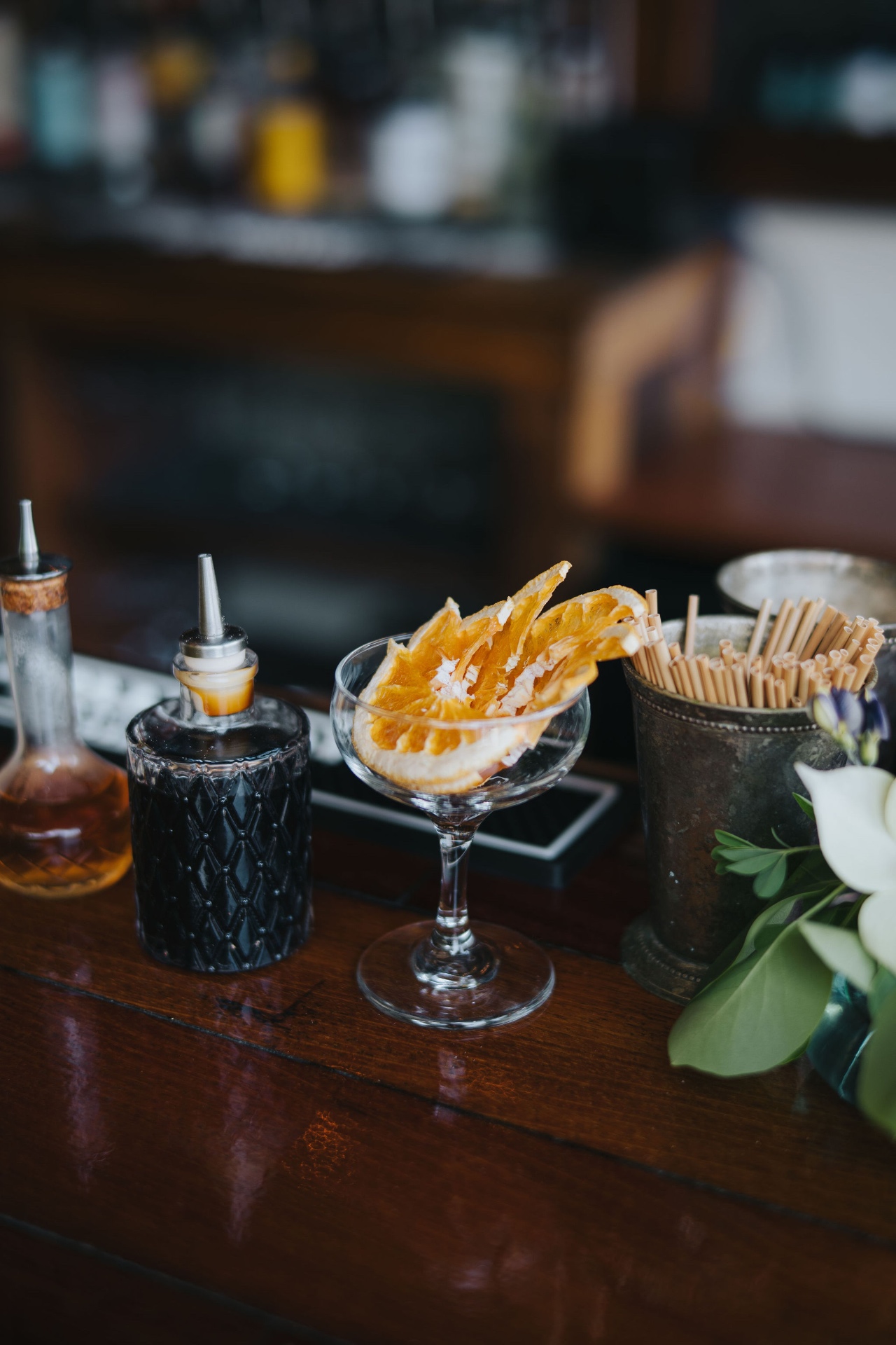 A coupe of dehydrated orange garnish beside a crystal bitters bottle