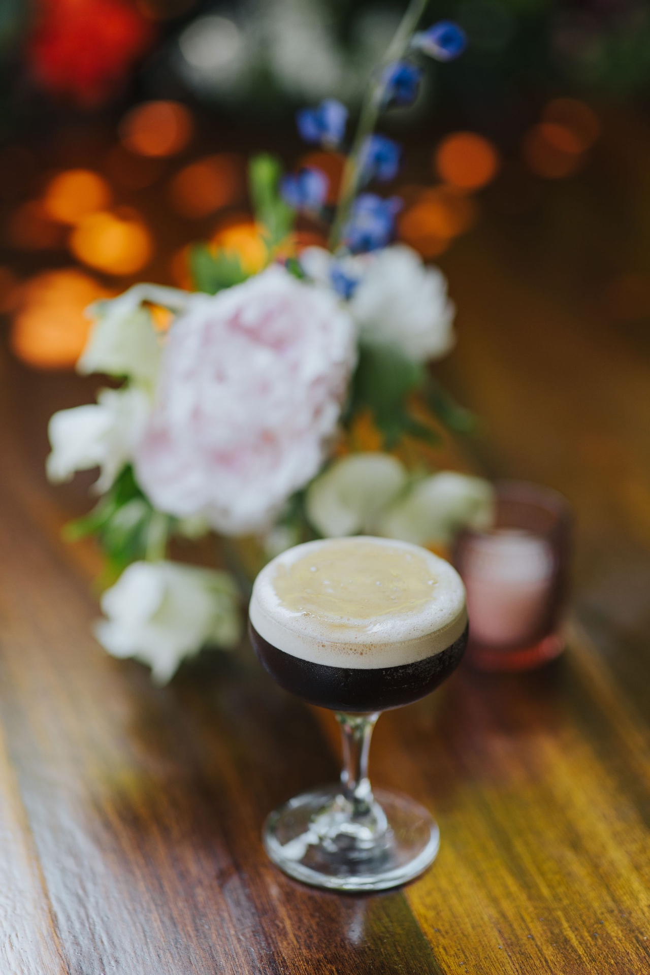 Espresso martini beside a bouquet of peonies and delphinium