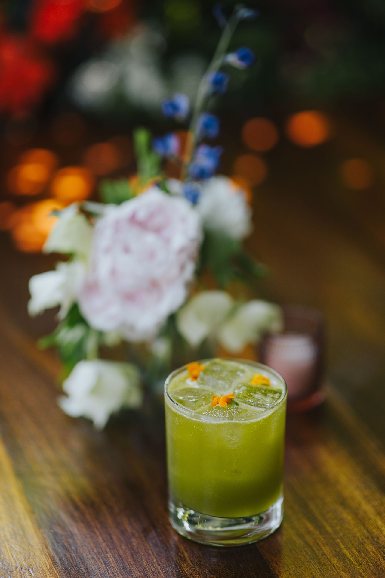 Green herbal cocktail beside a bouquet of peonies