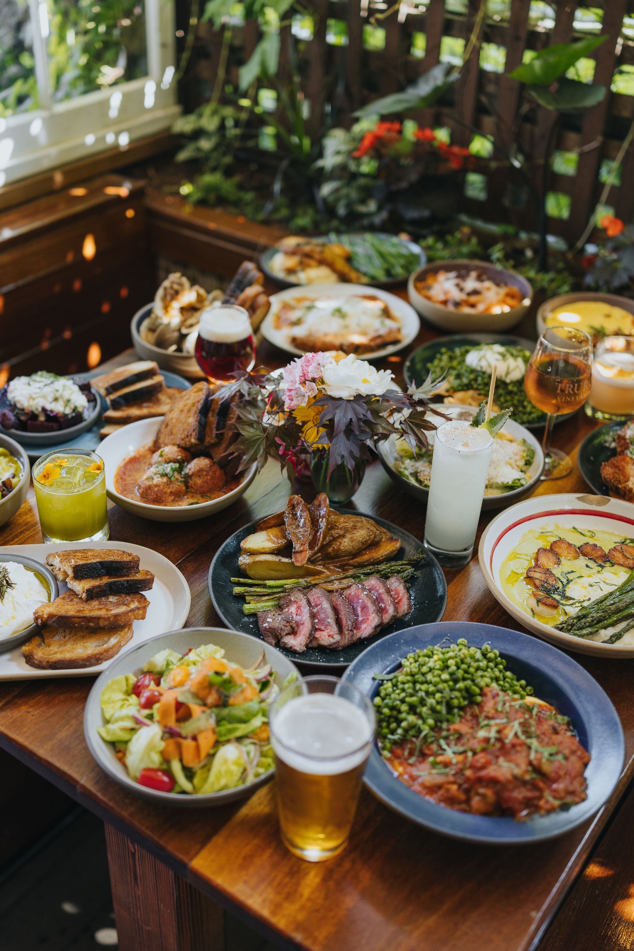 A table spread of beers, cocktails, and shared plates in the garden